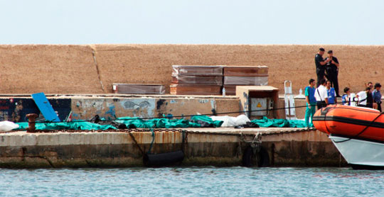 Policiais e voluntários de resgate italiano observam os corpos cobertos dos imigrantes no porto de Lampedusa