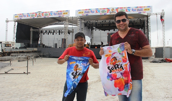 Marcinho da CLN ao lado de um funcionário apresenta a camisa do camarote (branca) e pista.